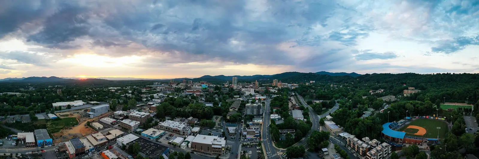 Aerial view of downtown Asheville at sunset, looking west toward the Blue Ridge Mountains.